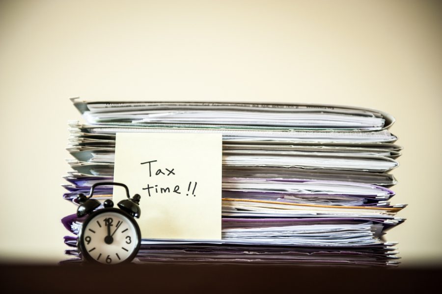 Traditional alarm clock in front of a stack of paper documents with handwritten tax time on a sticky note