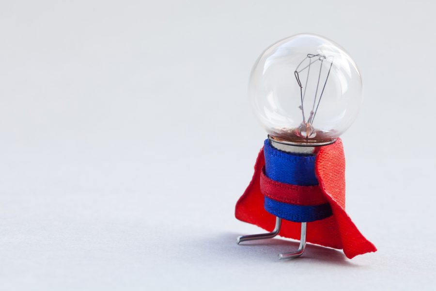 Light bulb superhero dressed in blue suit and red cape. Success man creative concept, fun, kind character. copy space, soft gray background